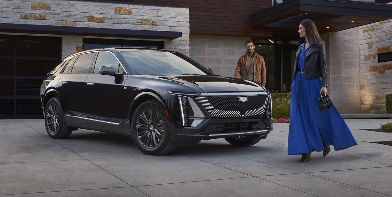 Um casal está em torno de um Cadillac Lyriq estacionado  em frente a uma casa, exibindo toda sua elegância.