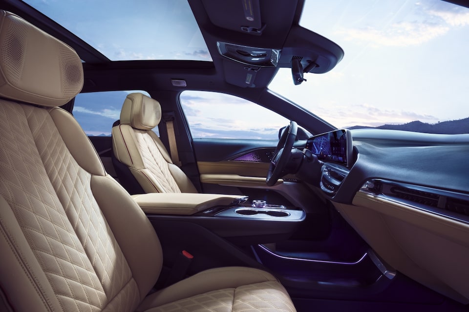 Visão lateral de um veículo Cadillac. No primeiro plano, o banco do passageiro. No segundo plano, banco do motorista, alavanca de câmbio, volante e central multimídia.