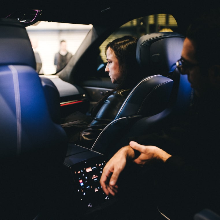 Visão interna, a partir da segunda fila, de um veículo Cadillac onde embarcados estão um homem (segunda fila) e uma mulher (primeira fila, assento do passageiro).
