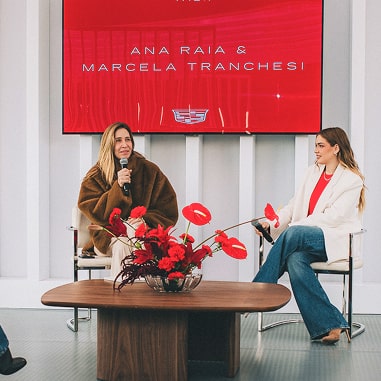 Duas mulheres estão sentadas dando uma palestra. As personalidades são: Ana Raia e Marcela Tranchesi.