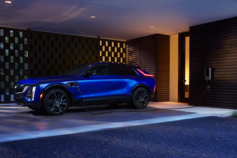 Veículo 100% elétrico da Cadillac em imagem ambientada; o SUV de luxo aparece estacionado na garagem de uma casa igualmente luxuosa.