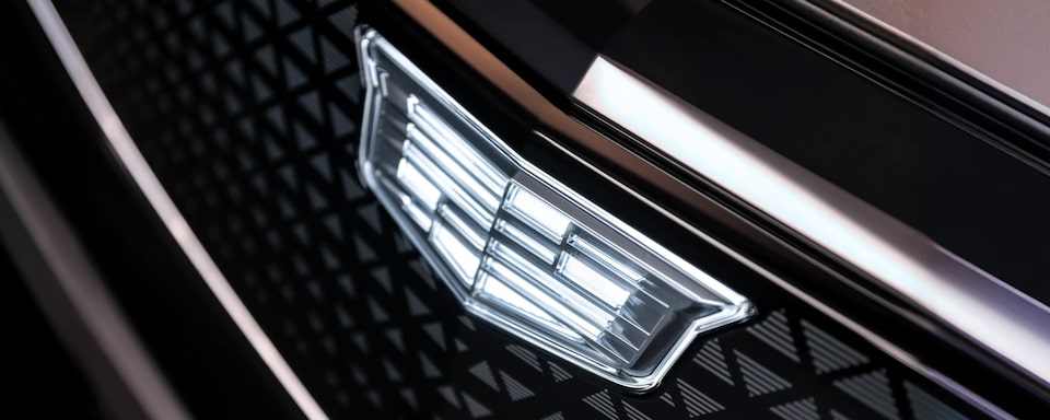 Emblema Cadillac aplicado na grade frontal do veículo em primeiro plano.