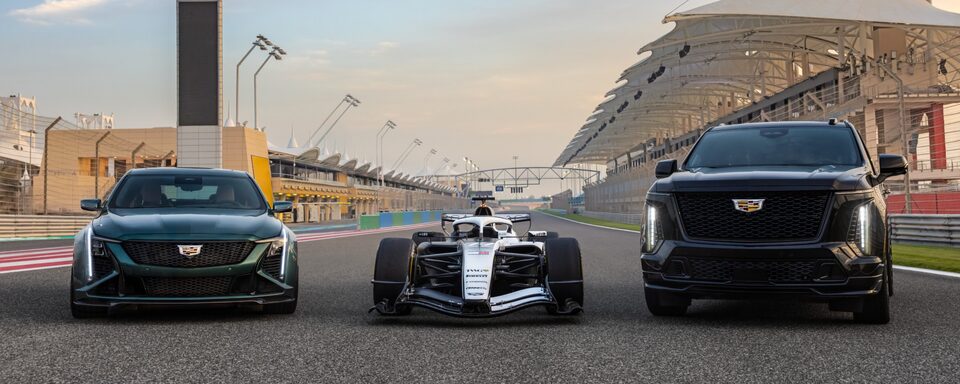 Trio de veículos Cadillac - um SUV, um F1 e um sedan de luxo - dispostos lado a lado em um autódromo.