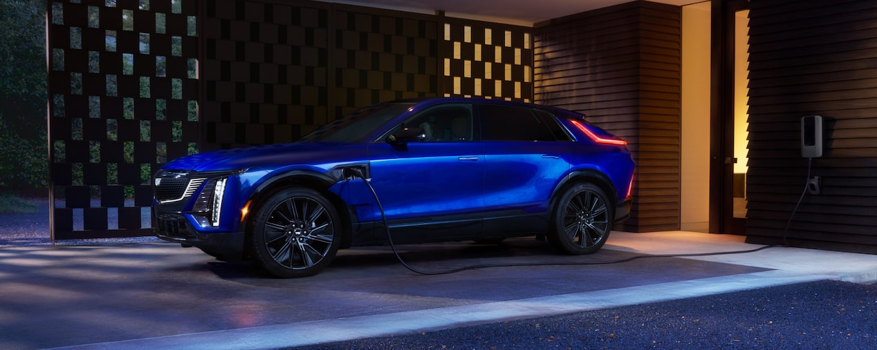 Veículo 100% elétrico da Cadillac em imagem ambientada; o SUV de luxo aparece estacionado na garagem de uma casa igualmente luxuosa.
