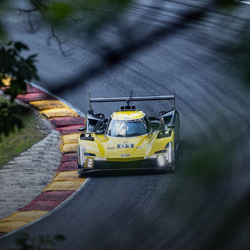 Carro de corrida Cadillac na cor amarela fazendo uma curva em alta velocidade, destacando-se na pista.