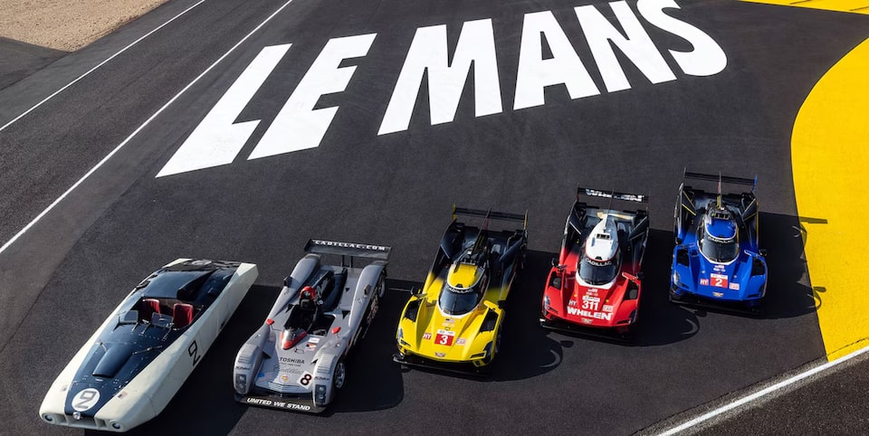 5 carros de corrida Cadillac posicionados em uma pista, com os dizeres da clássica corrida Le Mans logo atrás. 