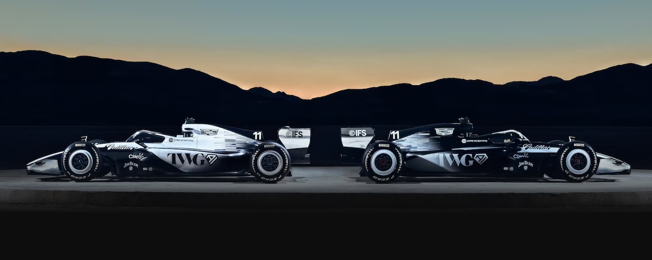 Dois carros da Cadillac Formula 1 Team estacionados um de costas para o outro sob o crepúsculo.