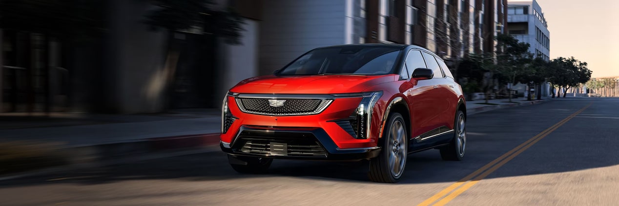 SUV elétrico Cadillac OPTIQ na cor vermelha em movimento por uma via urbana, exibido em visão frontal lateral, destacando o design esportivo, a iluminação em LED e as rodas de liga leve.