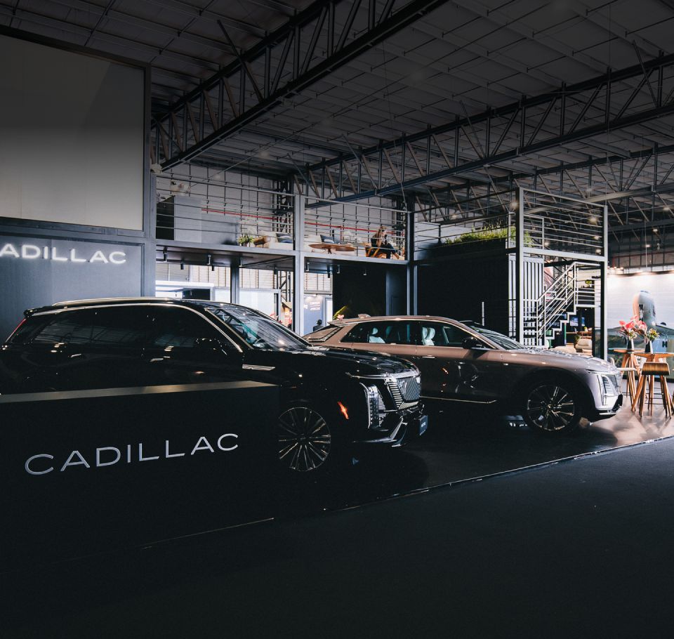 Estande da Cadillac com veículos da marca em exposição em um ambiente coberto e estrutura de um evento automotivo.