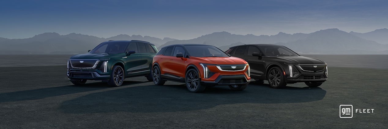Três carros elétricos da Cadillac posicionados lado a lado em um ambiente externo, incluindo um Cadillac VISTIQ na cor verde, um Cadillac OPTIQ na cor laranja e um Cadillac LYRIQ na cor preta, com montanhas ao fundo.