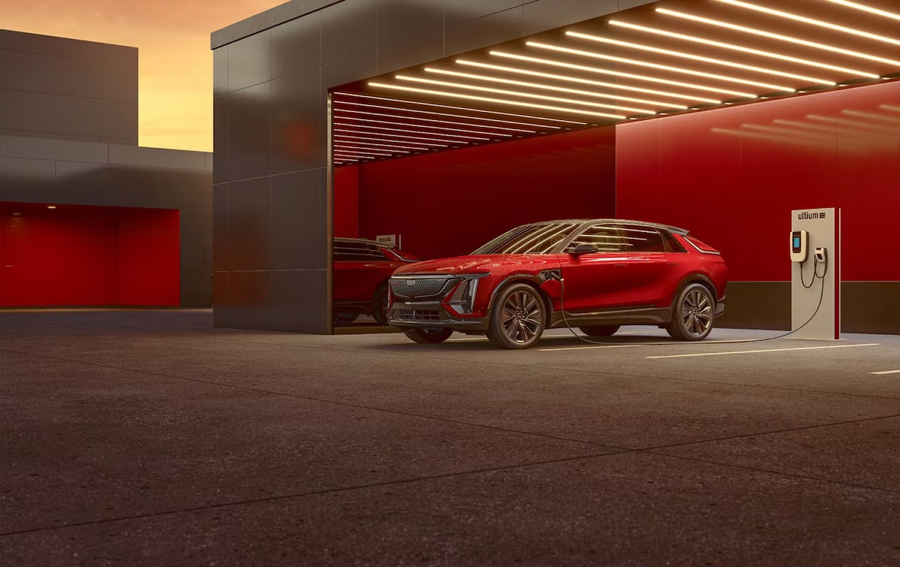 SUV elétrico Cadillac na cor vermelha estacionado ao lado de um carregador para veículos elétricos em um ambiente moderno, destacando o design sofisticado e a infraestrutura de recarga.