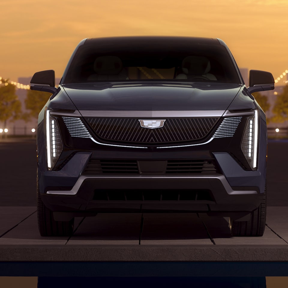 Visão frontal de um Cadillac Seville STS na cor preta, com seu design imponente e emblema marcante. 