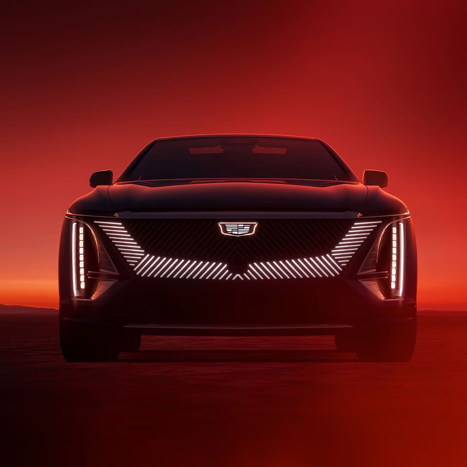 Frente de um veículo Cadillac moderno em um ambiente com luzes baixas e design impactante.