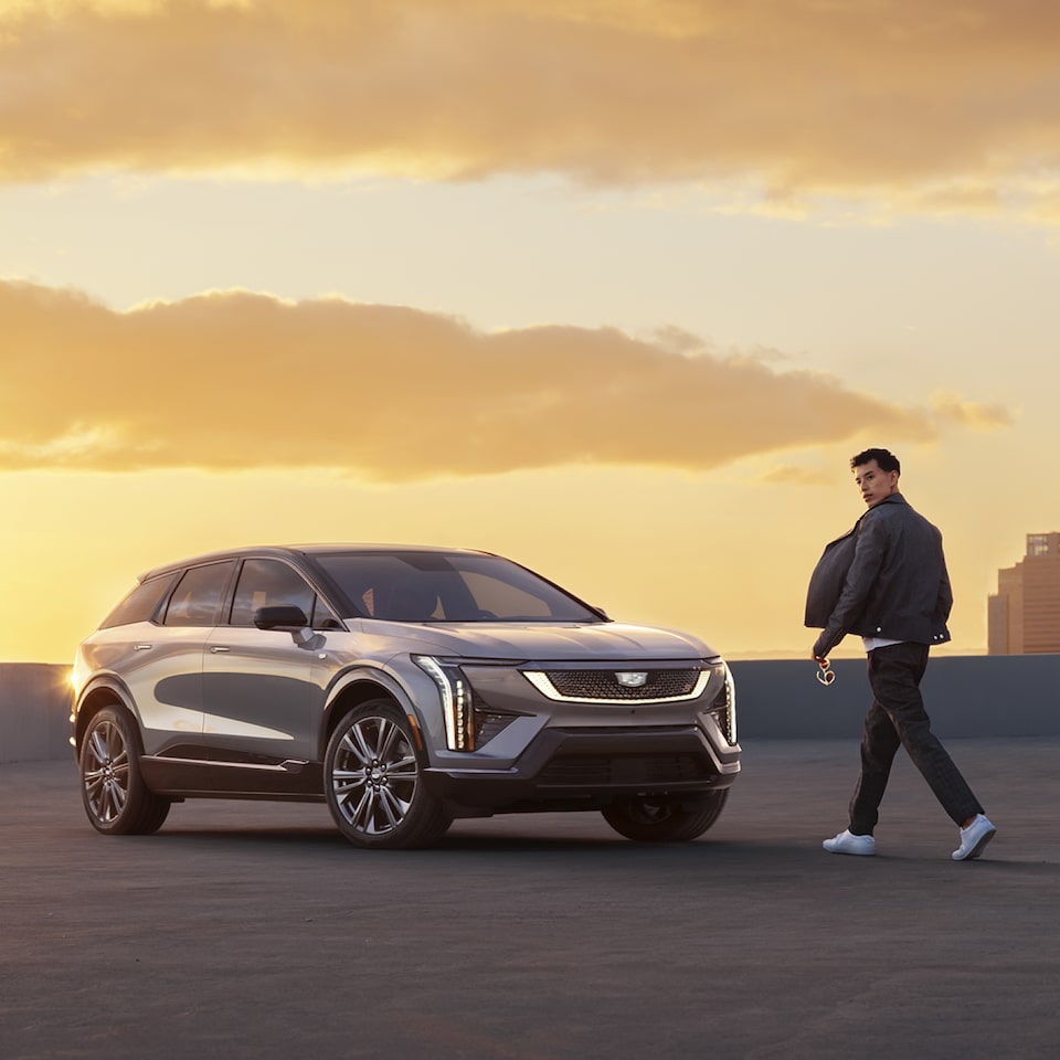 Homem caminha em direção a um Cadillac Optiq no pôr do sol. 