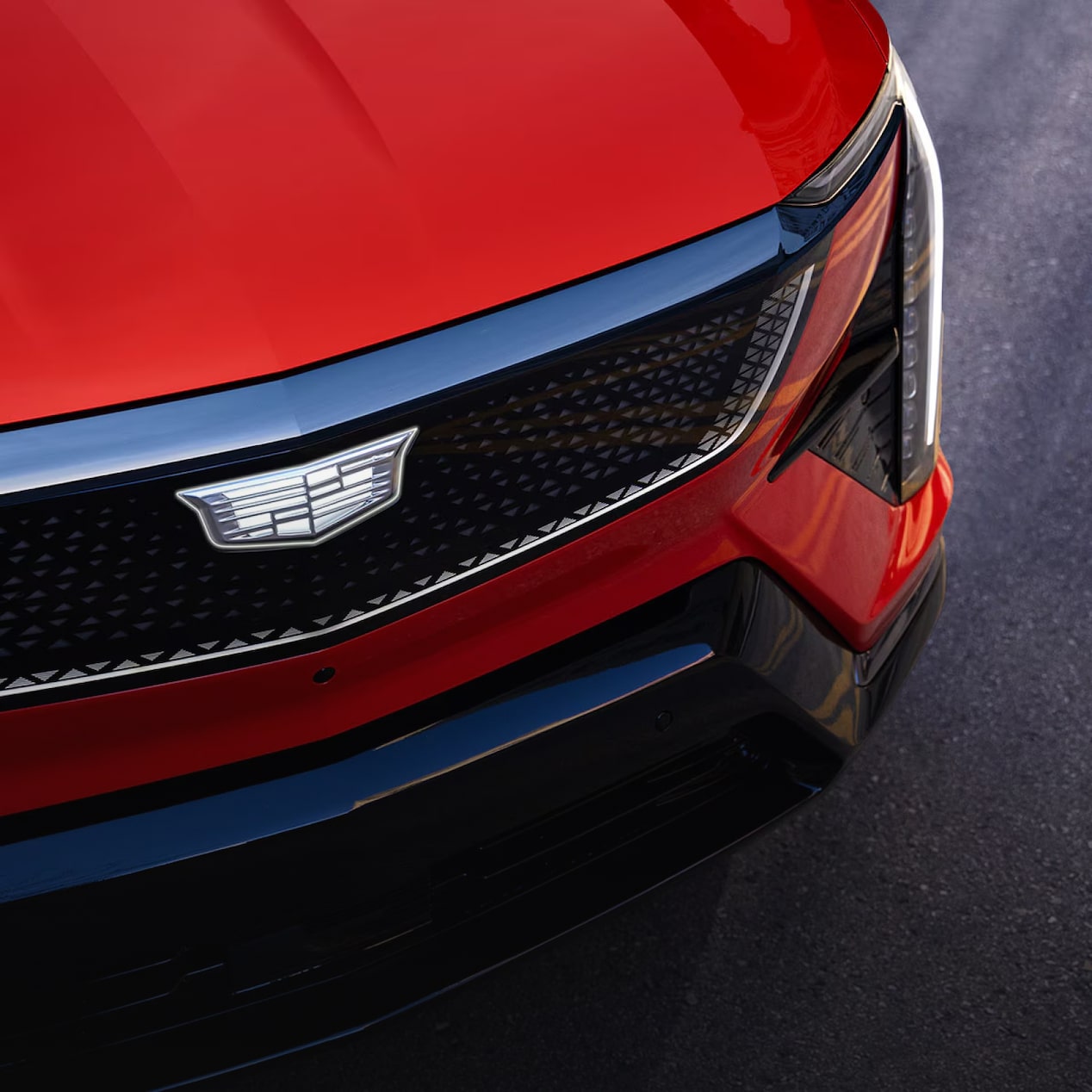 Detalhe da grade frontal do Cadillac Optiq na cor vermelha, destacando sua elegância e o emblema icônico da marca.