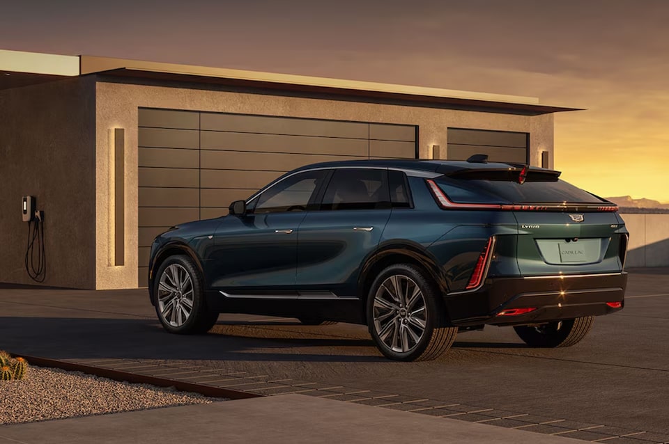 Cadillac Lyriq do lado de fora de uma garagem, com um carregador ao seu lado, mostrando a praticidade de se carregar de casa.