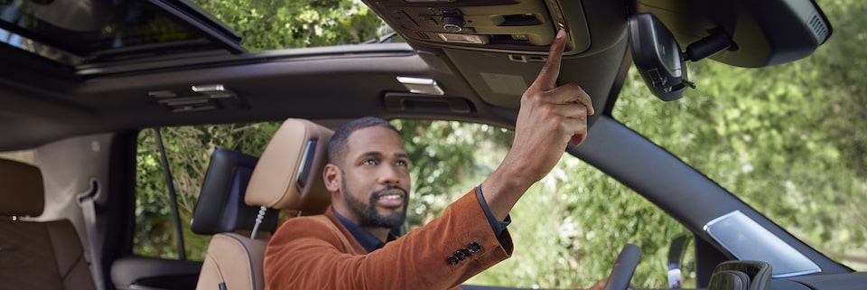 Homem dentro de um carro, com a mão no volante, e usufruindo dos comandos OnStar posicionados no painel superior de seu Cadillac. 