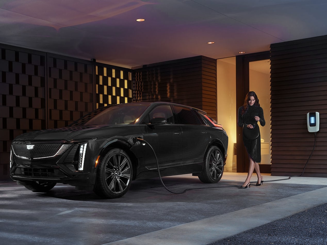 SUV elétrico Cadillac conectado a uma estação de recarga residencial, ilustrando a experiência de eletrificação e conveniência oferecida pela marca.