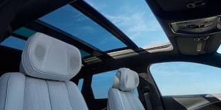 Interior do Cadillac LYRIQ com teto panorâmico de vidro, bancos dianteiros e painel tecnológico em destaque.
