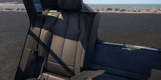 Cadillac LYRIQ na cor cinza em movimento, com vista frontal lateral, percorrendo uma estrada cercada por áreas verdes.