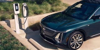 Cadillac LYRIQ na cor verde escuro conectado a um ponto de recarga para veículo elétrico em uma área externa.