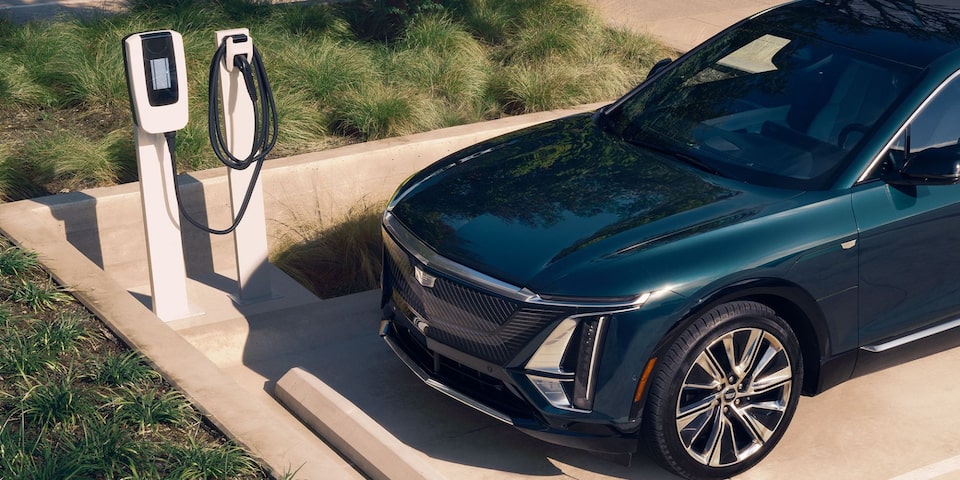 Cadillac LYRIQ na cor verde escuro conectado a um ponto de recarga para veículo elétrico em uma área externa.
