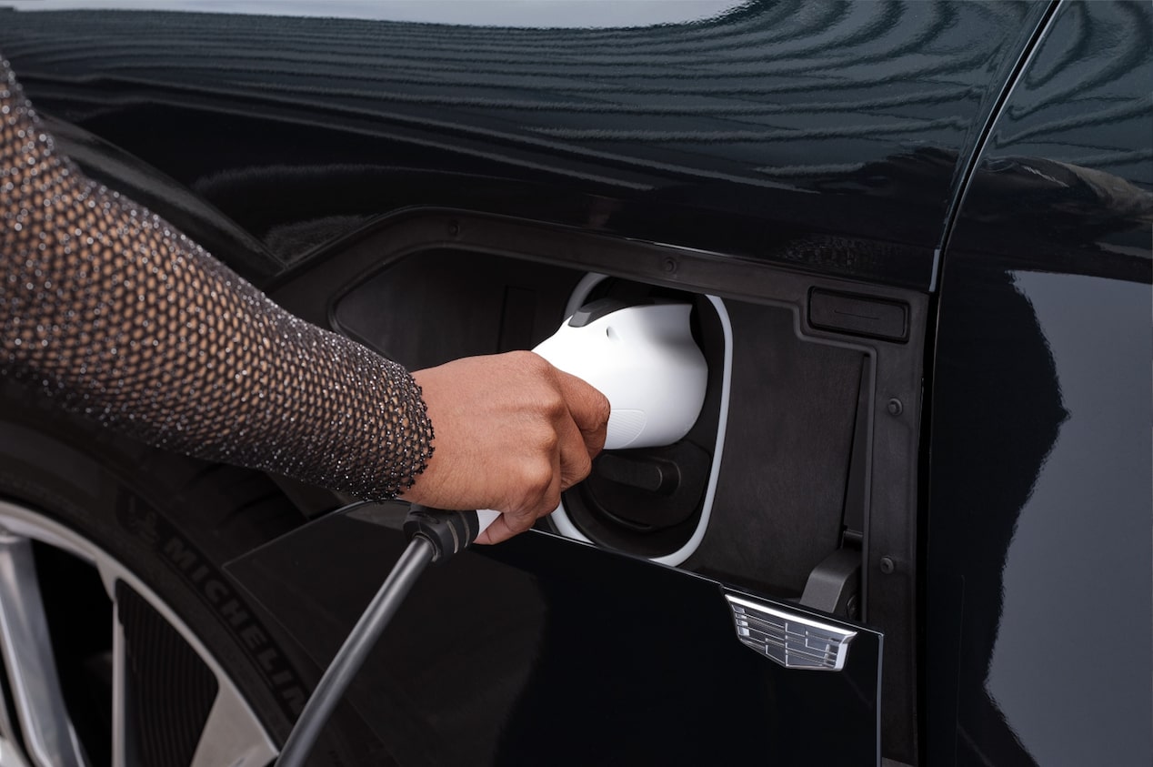 Mão feminina conecta o carregador wallbox em um veículo Cadillac.