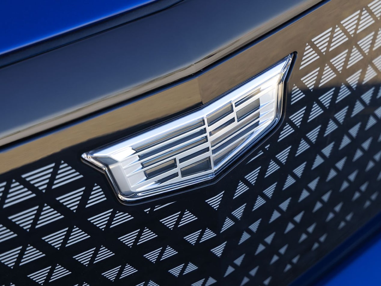 Detalhe da grade frontal de um veículo Cadillac na cor azul, destacando o emblema da marca e o acabamento com padrão geométrico.