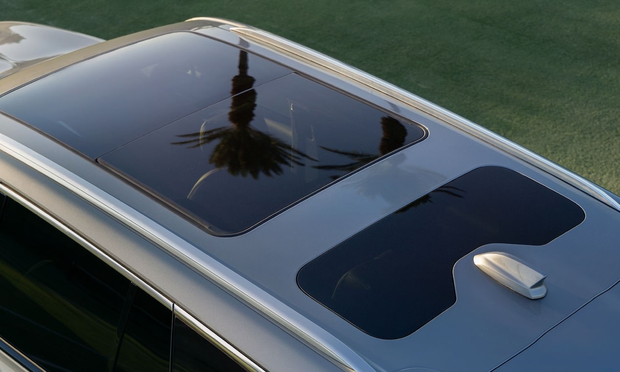 Interior de veículo Cadillac com bancos em couro branco, teto panorâmico de vidro e cabine ampla, destacando o acabamento premium e a iluminação natural.
