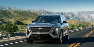 carro elétrico Cadillac na cor azul estacionado entre duas estações de carregamento para veículos elétricos, destacando o design moderno, as rodas de liga leve e a infraestrutura de recarga.