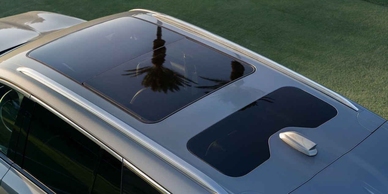 Vista superior de um veículo Cadillac destacando o teto panorâmico de vidro, com acabamento moderno e reflexo do ambiente externo.