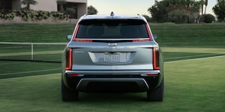Console central de veículo Cadillac com porta-copos, seletor de controle, tela multimídia integrada e acabamento premium em tons escuros.