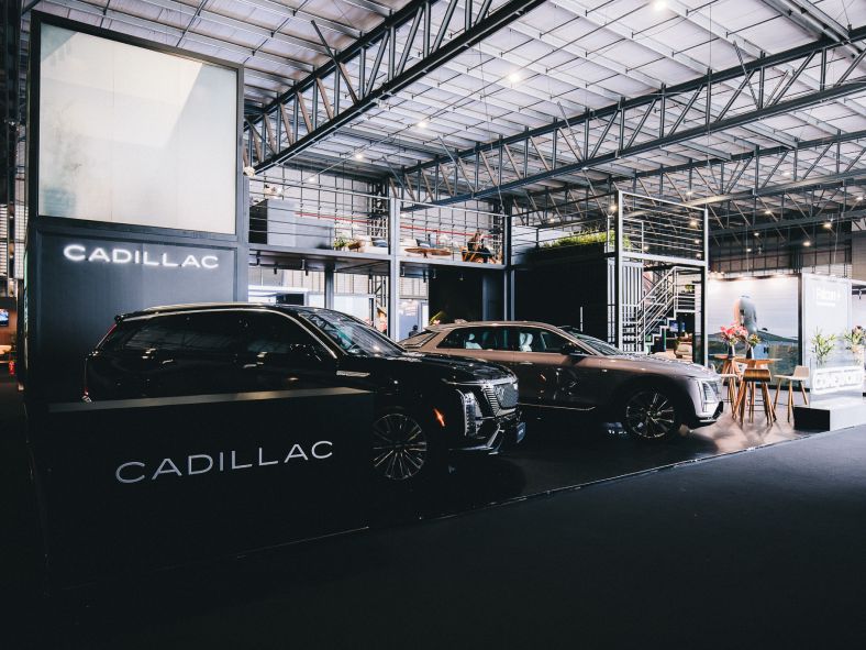 Estande da Cadillac com veículos da marca em exposição em um ambiente coberto, identidade visual da marca e estrutura de um evento automotivo.